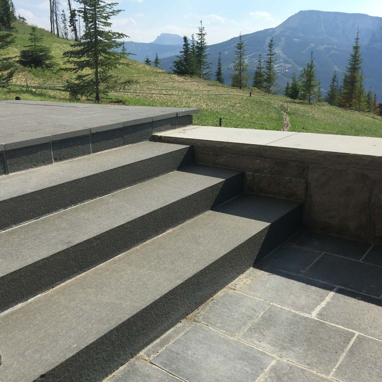 Application image for Nordic Black Basalt. The image shows this material being used for patio pavers and monolithic steps. The surface finish shown is flamed. Dominant colors shown are black and gray. The color mix creates a warm feeling. Regular color pattern.