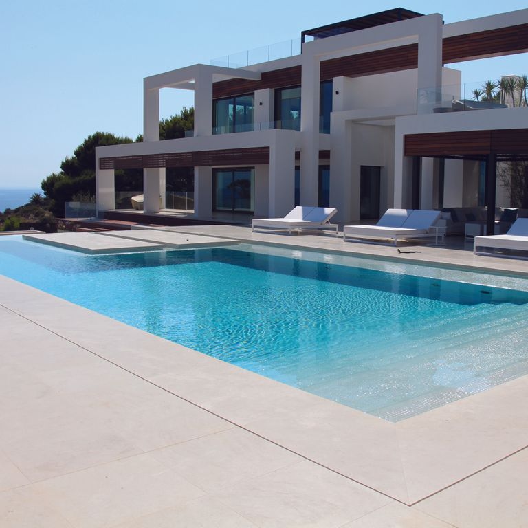 Feature image for Limestone - Portuguese Classic White. The image shows this material being used for pool coping and pool deck pavers. Dominant colors shown are beige, gray, white and cream; with a pink secondary. Solid and blotched color patterns.