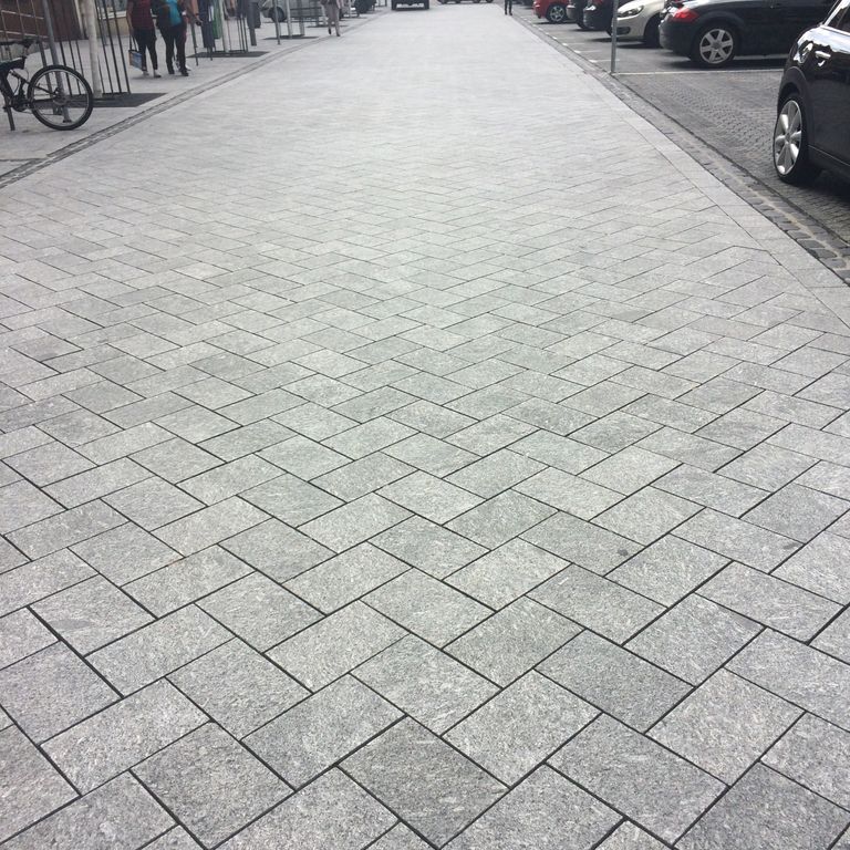 Feature image for Granite - Colonial Blue. The image shows this material being used for driveway pavers and public area. The dominant color shown is gray; with beige, black, pink, purple and white secondaries. Exhibits 