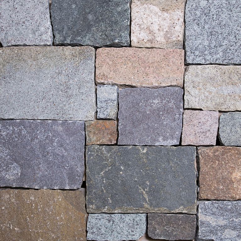 Best close-up image for Adirondack Granite. The image shows this material being used for full bed veneer and thin veneer. The surface finish shown is a combination of split-face, split-face with flat plane and weathered. The dominant color shown is gray; with beige, blue, brown, green, orange/rust, pink, purple, white and tan secondaries. Regular, fine speckled and cloudy color patterns.