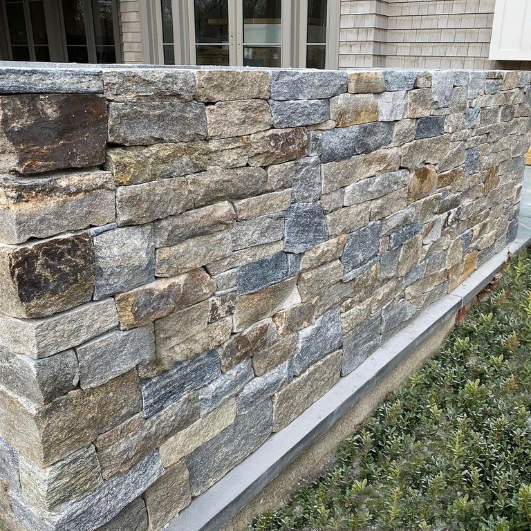 Feature image for Montauk Blend Granite. The image shows this material being used for landscape wallstone and full bed veneer. The surface finish shown is . The dominant color shown is gray; with blue, brown, green, orange/rust, purple and tan secondaries. Regular, linear and random color patterns.
