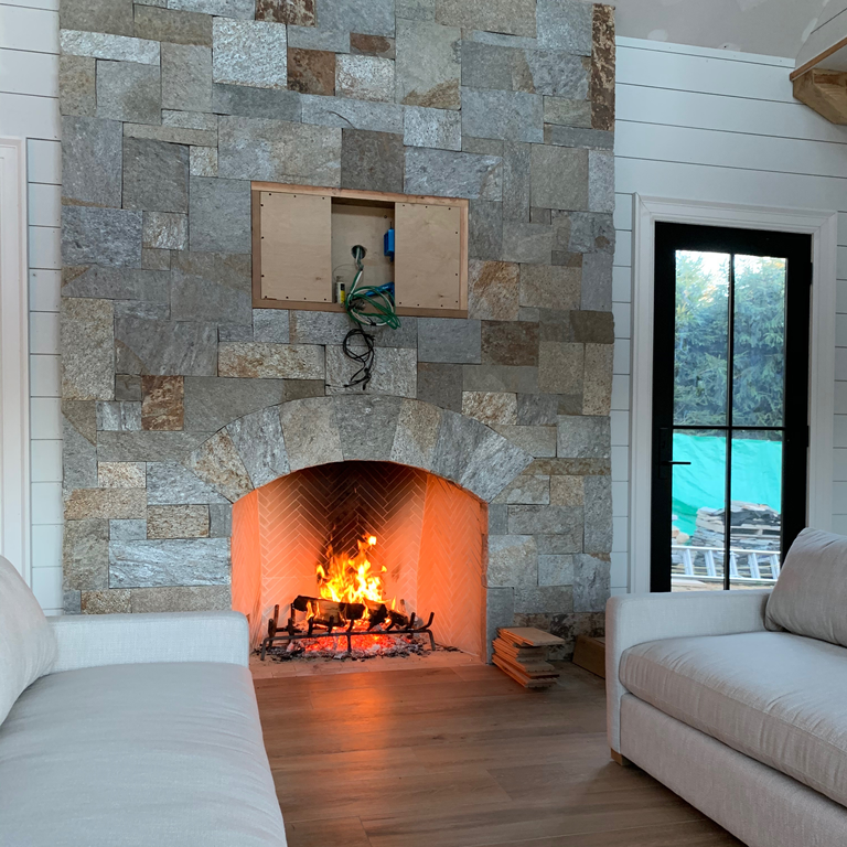 Feature image for Granite - Spruce Mountain. The image shows this material being used for fireplace surround, thin veneer and interior cladding. Dominant colors shown are beige, blue and gray; with brown and green secondaries. Exhibits 