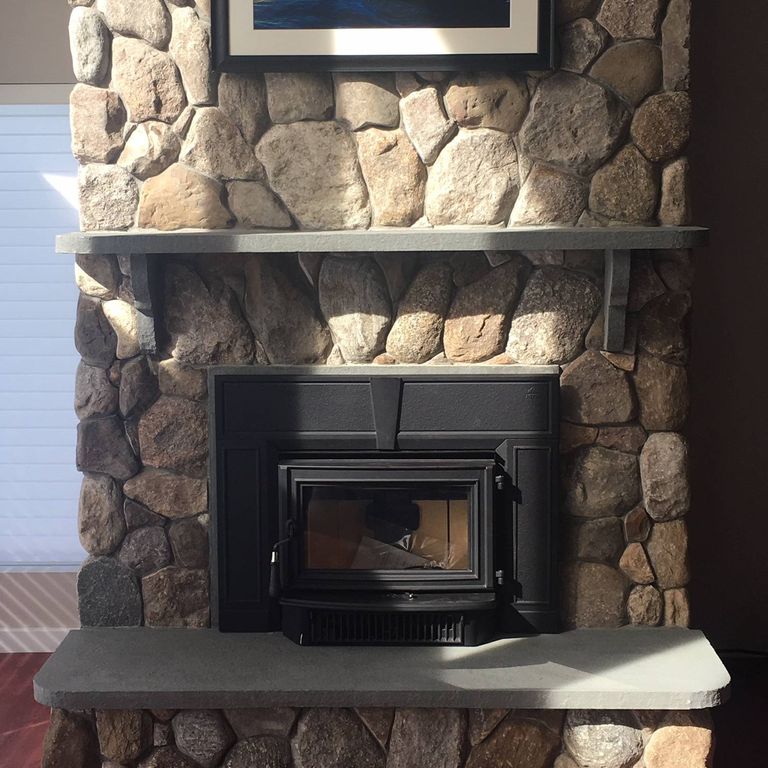 Application image for Fieldstone - Old New England Round. The image shows this material being used for fireplace mantel, thin veneer and interior cladding. Dominant colors shown are black and brown. The color mix creates a warm feeling.
