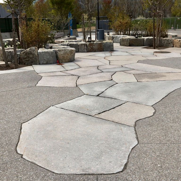 Feature image for Granite - New England Mix. The image shows this material being used for patio pavers and public area. The dominant color shown is gray; with beige, pink, white, tan and cream secondaries. The color mix creates a cool feeling. Speckled and cloudy color patterns.