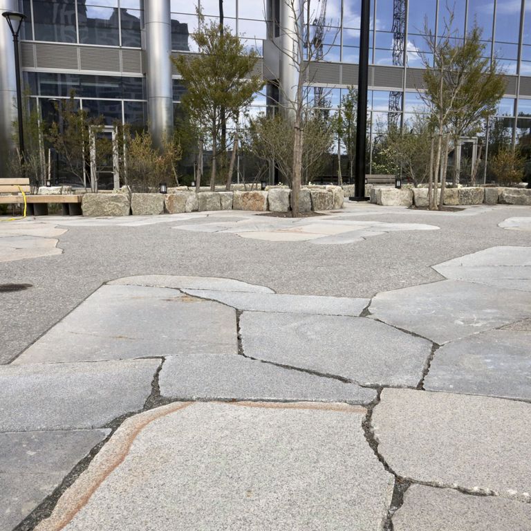 Application image for Granite - New England Mix. The image shows this material being used for patio pavers and public area. The dominant color shown is gray. The color mix creates a warm feeling.