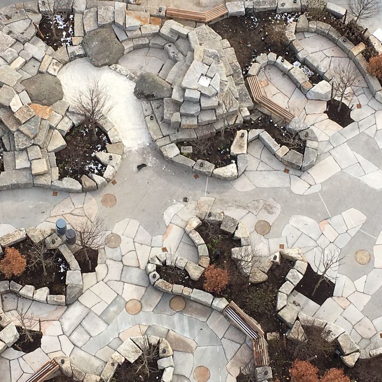 Application image for Granite - New England Mix. The image shows this material being used for patio pavers and public area. The dominant color shown is gray.