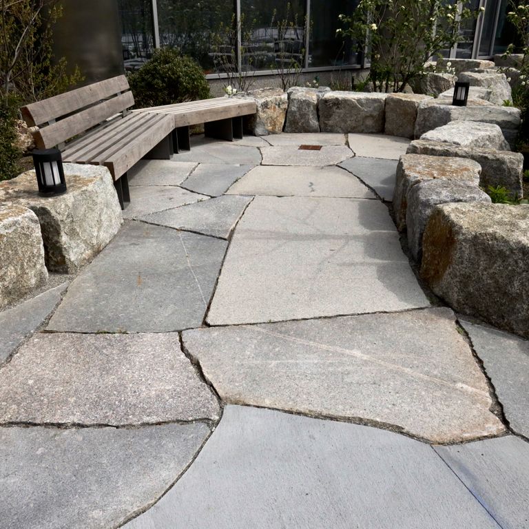 Application image for Granite - New England Mix. The image shows this material being used for patio pavers and public area. The dominant color shown is gray.