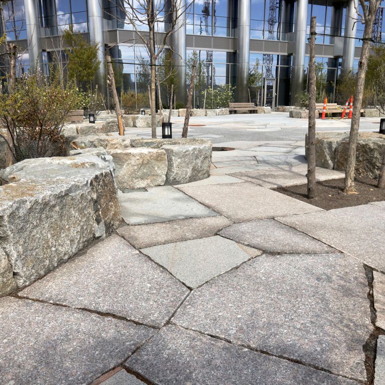 Application image for Granite - New England Mix. The image shows this material being used for patio pavers and public area. The dominant color shown is gray.