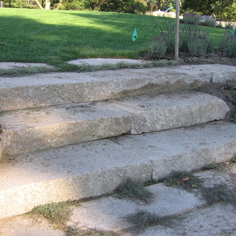 Application image for Millenium Granite. The image shows this material being used for path pavers and monolithic steps. The surface finish shown is a combination of flamed and split-face. The dominant color shown is gray. Fine speckled color pattern.