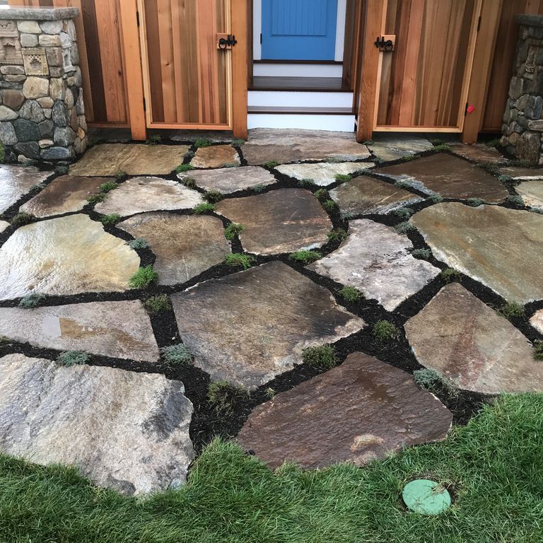 The image shows this material being used in a patio pavers application. The dominant color shown is gray; with beige, black, brown, orange/rust, purple, white and tan secondaries. Random color pattern.