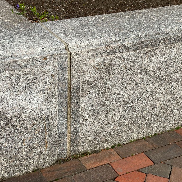 Feature image for Deer Isle Granite. The image shows this material being used in a landscape curbing & edging application. The surface finish shown is a combination of honed and split-face with flat plane. Dominant colors shown are gray and pink; with beige, white and cream secondaries. The color mix creates a warm feeling. Speckled and coarse speckled color patterns. Contains some mica and mineral inclusions.