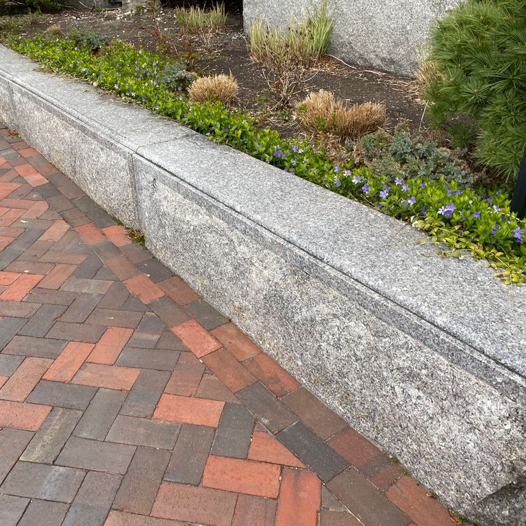 Application image for Deer Isle Granite. The image shows this material being used in a landscape curbing & edging application. The surface finish shown is a combination of honed and split-face with flat plane. Dominant colors shown are gray and pink. The color mix creates a warm feeling. Speckled and coarse speckled color patterns. Contains some mica and mineral inclusions.