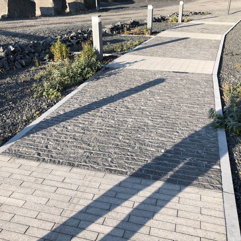 Application image for Limestone - Belgian Bluestone. The image shows this material being used in a path pavers application. The surface finish shown is a combination of sand blasted and split-face. The dominant color shown is gray. The color mix creates a warm feeling. Regular color pattern.