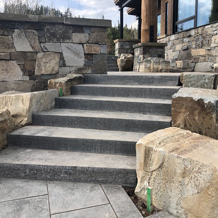 Application image for Highland Limestone. The image shows this material being used for patio pavers and monolithic steps. The surface finish shown is flamed. The dominant color shown is gray. Regular and random color patterns.