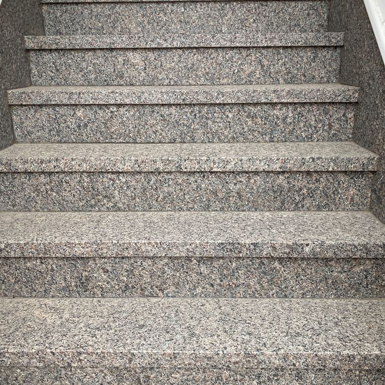 Application image for Granite - Caledonia. The image shows this material being used in a treads application. The surface finish shown is a combination of flamed and honed. The dominant color shown is gray. The color mix creates a warm feeling. Coarse speckled color pattern.