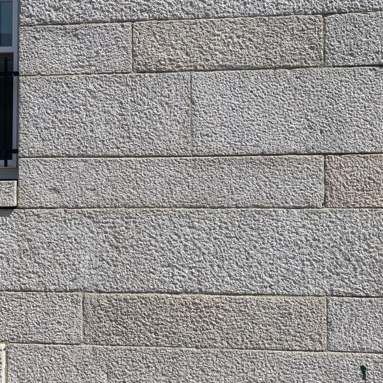 Application image for Chelmsford Gray Granite. The image shows this material being used in a full bed veneer application. The surface finish shown is coarse bush hammered. The dominant color shown is gray. The color mix creates a cool feeling. Speckled color pattern.