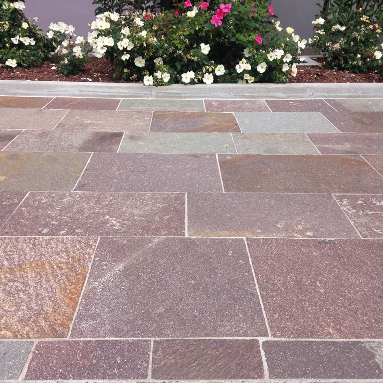 Feature image for Porphyry - Natural Surface - Mixed Red. The image shows this material being used in a patio pavers application. Dominant colors shown are gray, orange/rust and purple; with beige, brown, green, pink and tan secondaries. Exhibits 