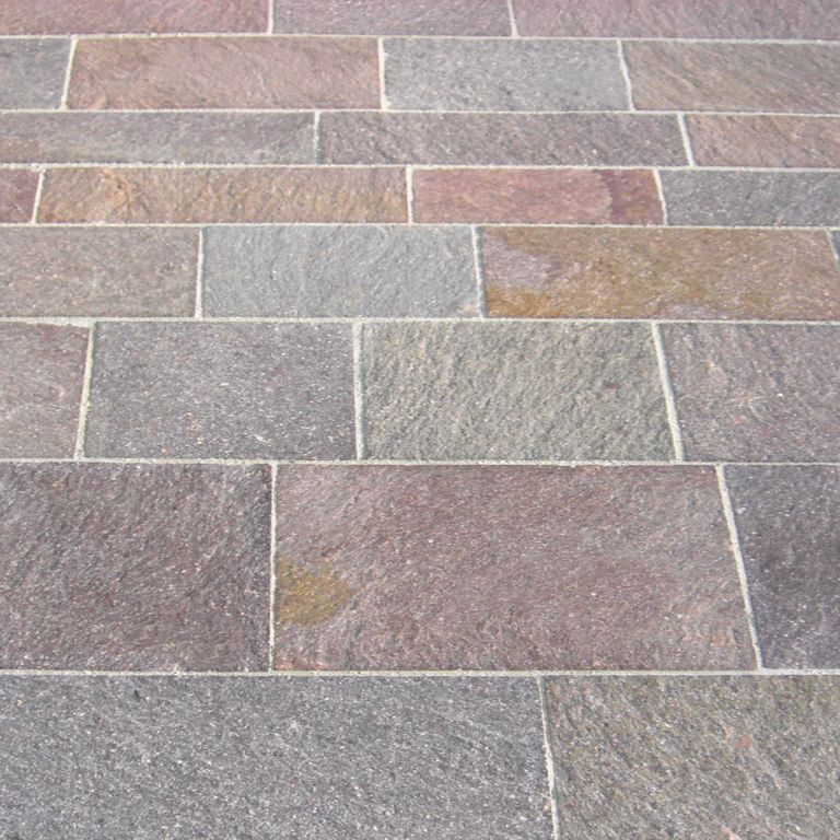 Application image for Porphyry - Natural Surface - Mixed Color. The image shows this material being used for driveway pavers, path pavers and patio pavers. Dominant colors shown are brown, green, gray, orange/rust, purple and red. The color mix creates a warm feeling. Streaked and speckled color patterns.
