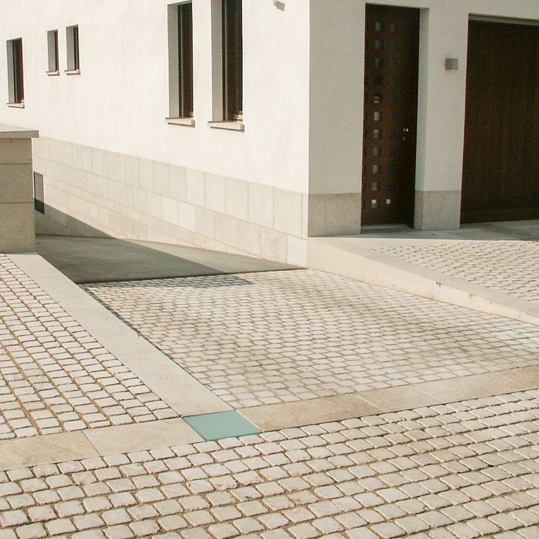 Application image for Bavarian Limestone - Beige. The image shows this material being used for driveway pavers, patio pavers and driveway aprons. The surface finish shown is tumbled. Dominant colors shown are beige and tan. The color mix creates a warm feeling. Solid color pattern.