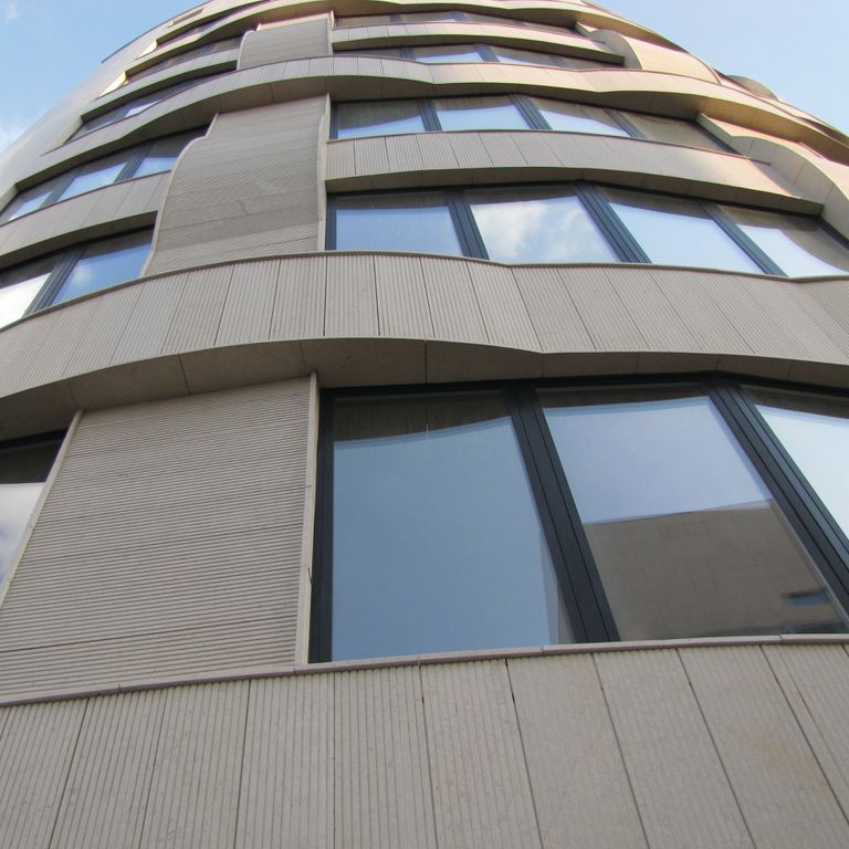 Feature image for Sona Beige Limestone. The image shows this material being used in a thin veneer application. Dominant colors shown are beige and gray; with a tan secondary. The color mix creates a warm feeling. Regular, linear and cloudy color patterns. Contains mineral inclusions.