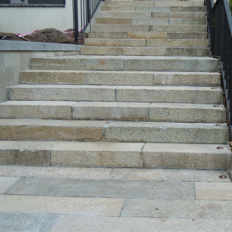 Feature image for Reclaimed Granite Stair Blocks. The image shows this material being used in a monolithic steps application. The dominant color shown is gray; with beige, blue, brown, green, orange/rust, purple, white and tan secondaries. Exhibits 