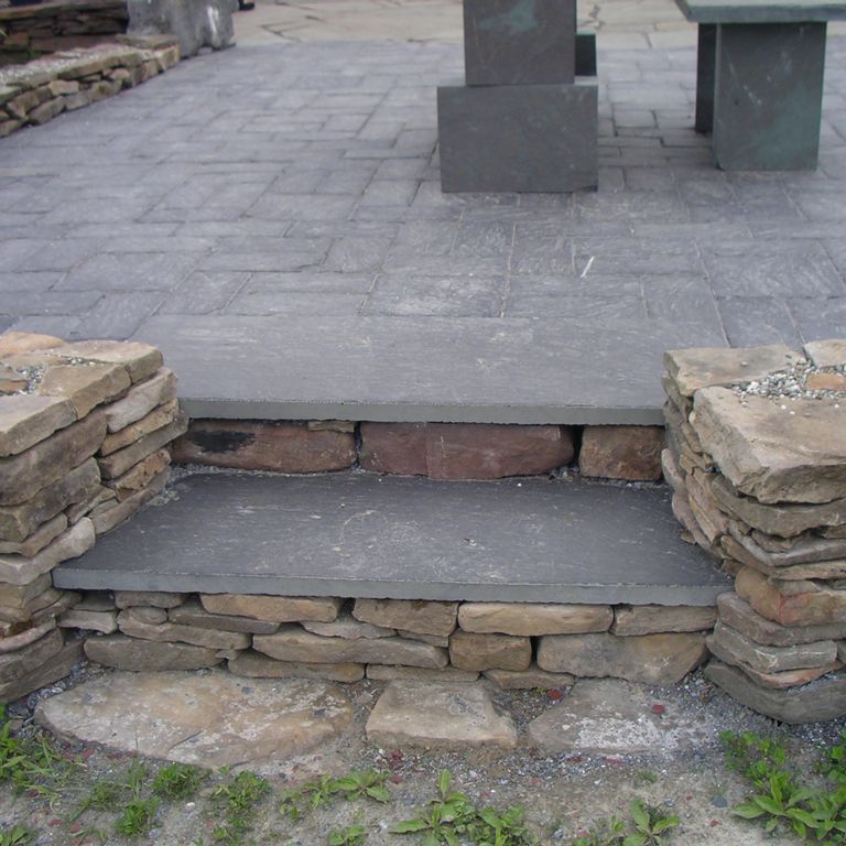 Feature image for Vermont Slate - Black. The image shows this material being used for patio pavers and treads. The dominant color shown is gray; with black and purple secondaries. The color mix creates a cool feeling. Regular and cloudy color patterns.