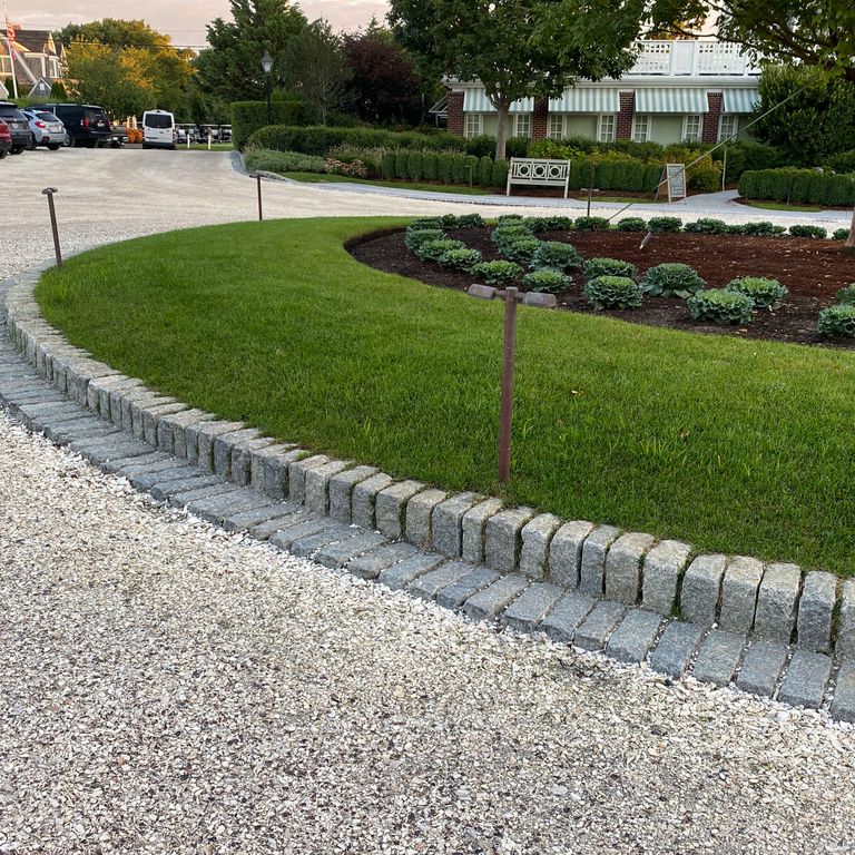 Application image for Granite Cobblestones - Gray. The image shows this material being used in a landscape curbing & edging application. This is a landscape stone for outdoor commercial and residential applications. Suitable for general use, freeze-thaw conditions, low heat absorption surfaces, high traffic areas and low slipperiness surfaces situations. Relatively moderate in price.