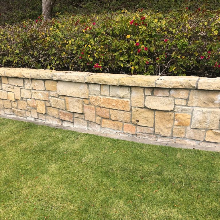 Application image for Honey Buff Limestone. The image shows this material being used for wallstone cap, full bed veneer and thin veneer. The surface finish shown is split-face. Dominant colors shown are gray and tan; with a brown secondary. The color mix creates a warm feeling. Regular color pattern.