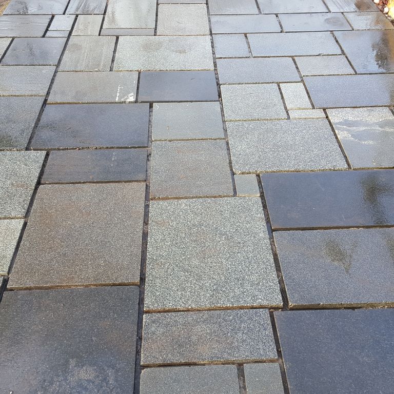 Feature image for Reclaimed European Granite. The image shows this material being used for path pavers and patio pavers. The dominant color shown is gray; with blue, brown, green, purple and white secondaries. The color mix creates a warm feeling. Speckled and blotched color patterns.