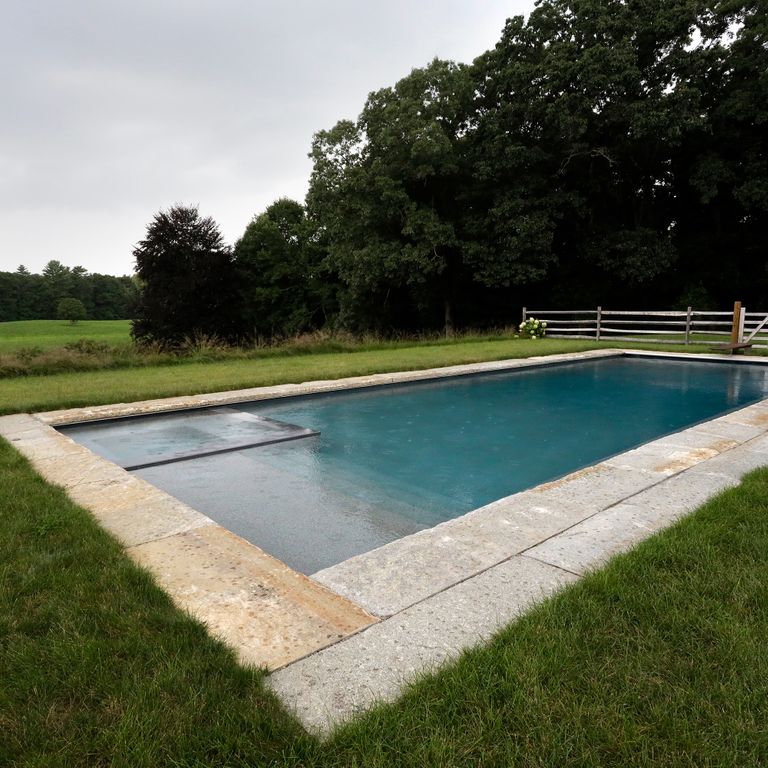 Application image for Reclaimed First Generation Granite Curbstone. The image shows this material being used for pool coping and pool deck pavers. The surface finish shown is a combination of weathered and worn. The dominant color shown is gray; with beige, brown and orange/rust secondaries. The color mix creates a warm feeling. Speckled and blotched color patterns.