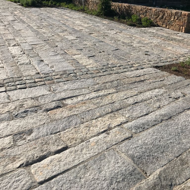 Application image for Granite - Reclaimed First Generation Curbstone. The image shows this material being used in a driveway pavers application. The dominant color shown is gray; with beige, brown and white secondaries. Regular color pattern.