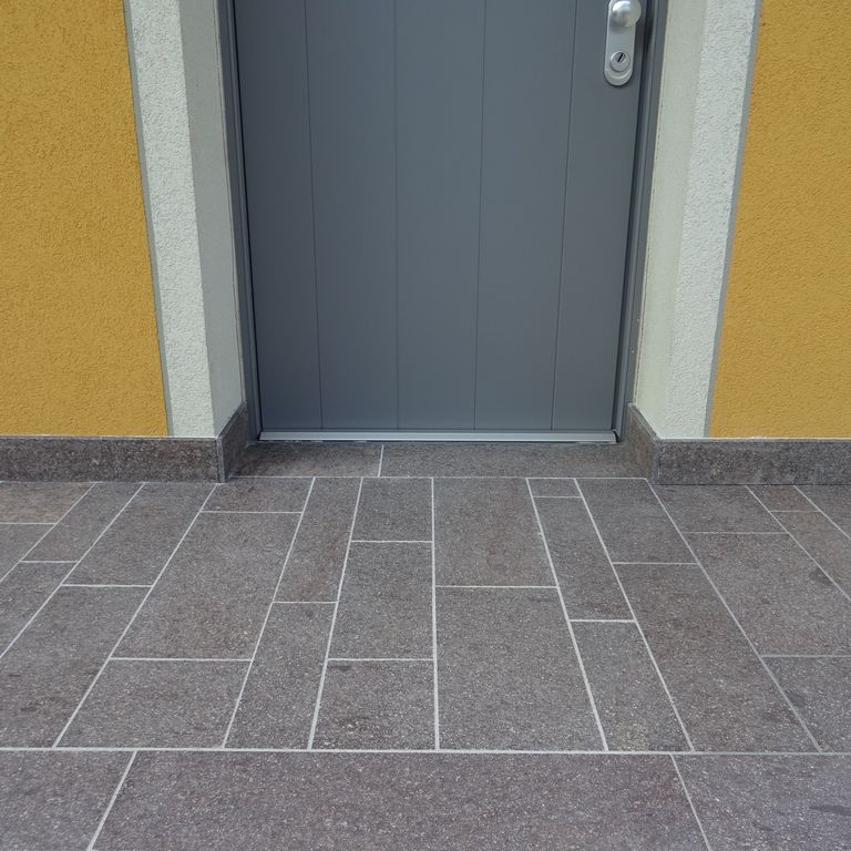 Application image for Porphyry - Imperial Roman Brown. The image shows this material being used in a patio pavers application. The surface finish shown is flamed. Dominant colors shown are brown and gray. The color mix creates a cool feeling.