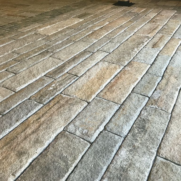 The image shows this material being used for interior floor and driveway pavers. The dominant color shown is gray; with beige, brown and orange/rust secondaries.