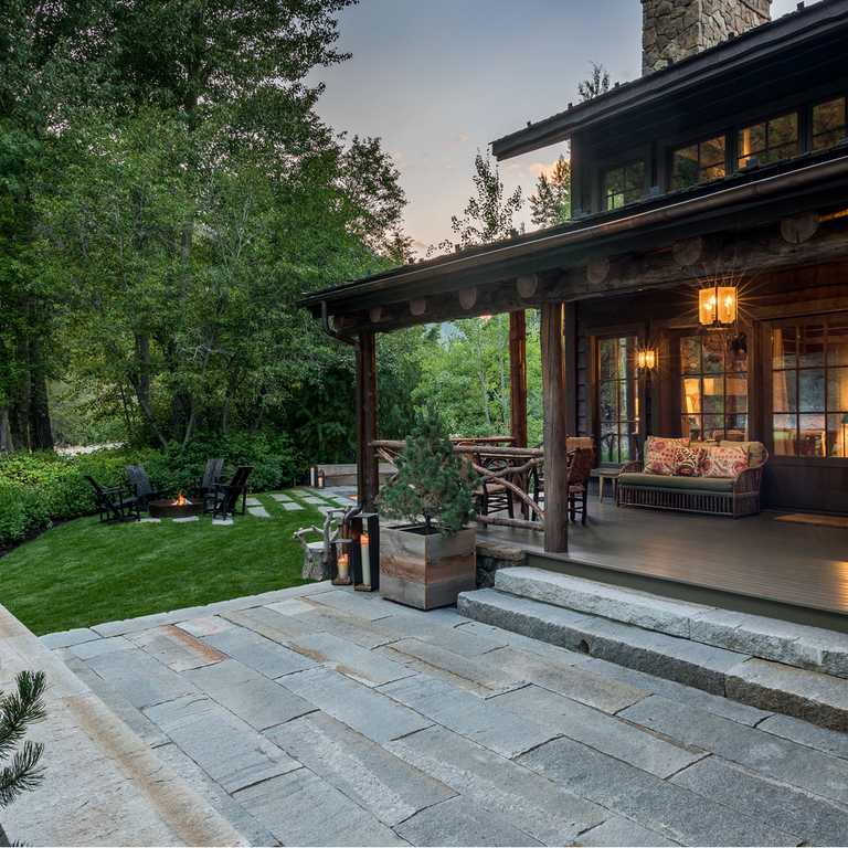 Application image for Reclaimed Third Generation Granite Curbstone. The image shows this material being used in a patio pavers application. The surface finish shown is a combination of weathered and worn. The dominant color shown is gray; with an orange/rust secondary. The color mix creates a cool feeling. Speckled color pattern.
