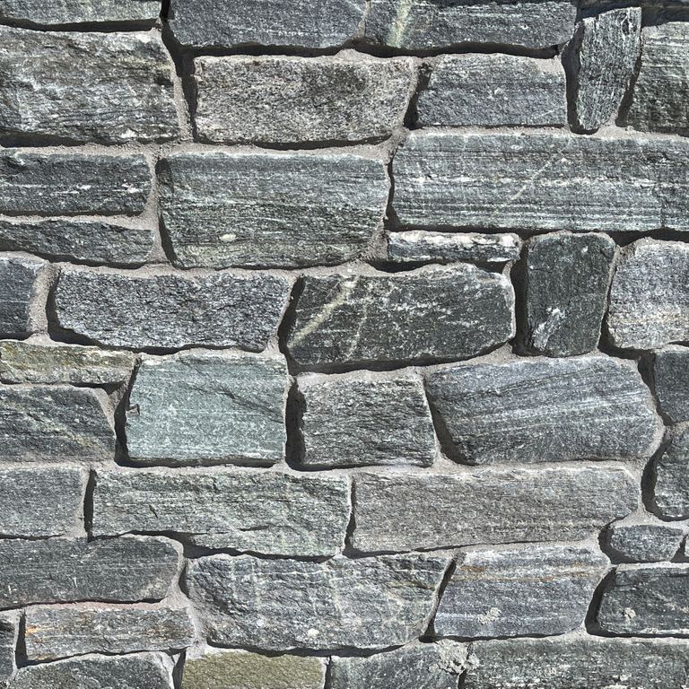 Best close-up image for Connecticut White Line Granite. The image shows this material being used in a landscape wallstone application. The surface finish shown is split-face. Dominant colors shown are gray and white; with blue, green and white secondaries. Exhibits 