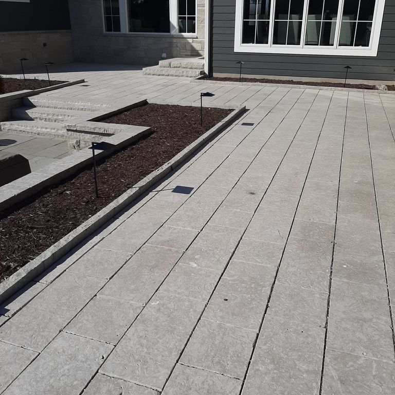 Application image for Madison Limestone. The image shows this material being used for wallstone cap, landscape curbing & edging, patio pavers and monolithic steps. The surface finish shown is flamed. The dominant color shown is gray; with beige, blue, brown, purple and white secondaries. The color mix creates a cool feeling. Regular color pattern.