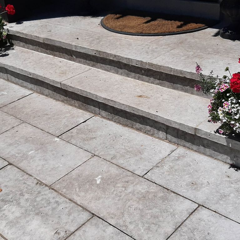 Application image for Madison Limestone. The image shows this material being used for path pavers, patio pavers and treads. The surface finish shown is flamed. The dominant color shown is gray; with beige, blue, purple and white secondaries. The color mix creates a cool feeling. Regular color pattern.