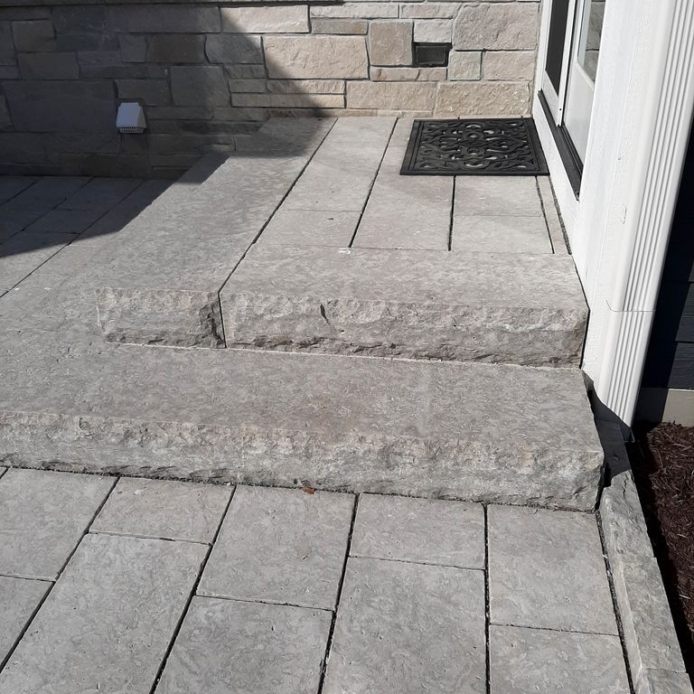 Application image for Madison Limestone. The image shows this material being used for landscape curbing & edging, patio pavers and monolithic steps. The surface finish shown is flamed. The dominant color shown is gray; with beige, blue, purple and white secondaries. The color mix creates a cool feeling. Regular color pattern.