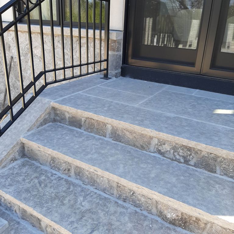 Application image for Limestone - Madison. The image shows this material being used for wallstone cap, patio pavers and treads. The surface finish shown is flamed. Dominant colors shown are blue and gray; with beige, white, tan and cream secondaries. The color mix creates a cool feeling. Regular color pattern.