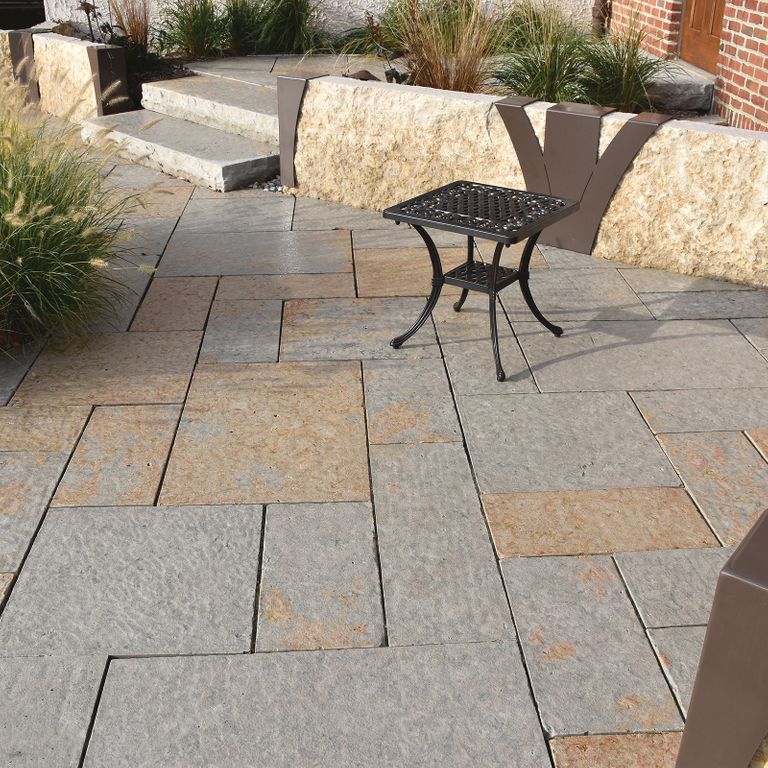 Application image for Beaver Creek Limestone - Full Color. The image shows this material being used for landscape wallstone and monolithic steps. The surface finish shown is a combination of flamed, rockfaced and split-face. Dominant colors shown are brown, gray and tan; with beige, orange/rust and cream secondaries. Random color pattern. Contains voids.