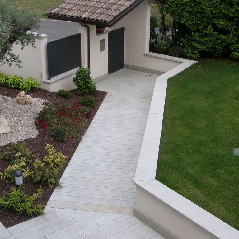 Feature image for Veneto Olivo Limestone - Pavers. The image shows this product being used in a path pavers application. The surface finish shown is flamed. Dominant colors shown are beige, gray and tan. The color mix creates a warm feeling.