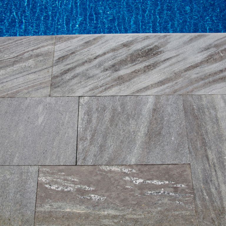 Application image for Granite - Mystic Mountain- Dimensional Cut Pavers. The image shows this product being used for pool coping and pool deck pavers. The surface finish shown is flamed. The dominant color shown is gray; with green and purple secondaries. The color mix creates a cool feeling. Streaked color pattern.