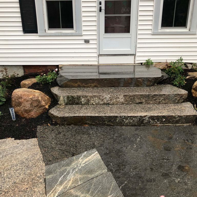 Application image for New England Fieldstone Boulders - Sawn - Live Edge Step. The image shows this product being used in a monolithic steps application. Dominant colors shown are black, brown and gray.