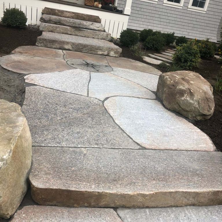 Feature image for New England Fieldstone Boulders - Sawn Pavers. The image shows this product being used in a path pavers application. The design pattern shown is irregular flagging sawn flat edges & irregular sawn edges. Dominant colors shown are gray and tan; with beige, brown, orange/rust, pink, purple, white and cream secondaries. The color mix creates a warm feeling. Speckled, fine speckled, blotched and cloudy color patterns.
