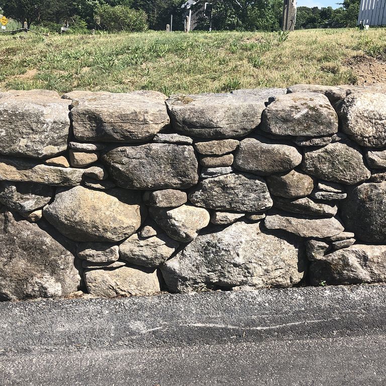 Application image for New England Fieldstone - Wallstone Run Mix. The image shows this product being used in a landscape wallstone application. The surface finish shown is weathered. The dominant color shown is gray.