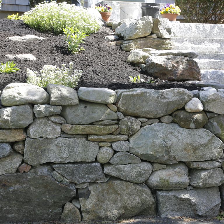 Application image for New England Fieldstone - Wallstone Run Mix. The image shows this product being used in a landscape wallstone application. The surface finish shown is weathered. The dominant color shown is gray.