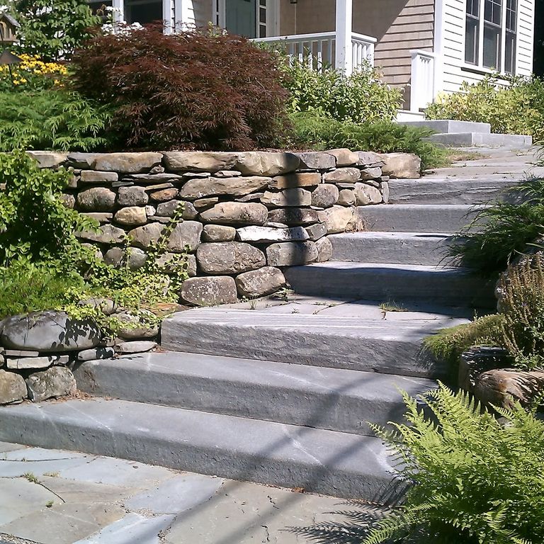 Application image for New England Fieldstone - Wallstone Run Mix. The image shows this product being used in a landscape wallstone application. The surface finish shown is weathered. The dominant color shown is gray.