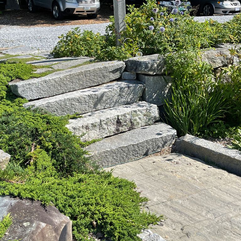 Application image for Reclaimed First Generation Granite Curbstone Steps - Textured Riser and Tread. The image shows this product being used in a monolithic steps application. The surface finish shown is a combination of weathered and worn. The dominant color shown is gray. The color mix creates a cool feeling.