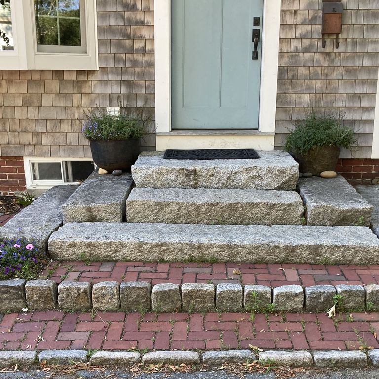 Application image for Reclaimed First Generation Granite Curbstone Steps - Textured Riser and Tread. The image shows this product being used in a monolithic steps application. The surface finish shown is a combination of weathered and worn. The dominant color shown is gray; with beige, blue, brown and tan secondaries. The color mix creates a cool feeling. Speckled color pattern.
