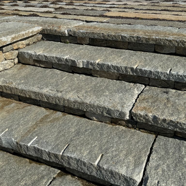 Best close-up image for Reclaimed Granite Treads - Weathered Riser and Tread. The image shows this product being used in a treads application. The surface finish shown is . The dominant color shown is gray; with green, orange/rust and purple secondaries. The color mix creates a warm feeling. Speckled and random color patterns.